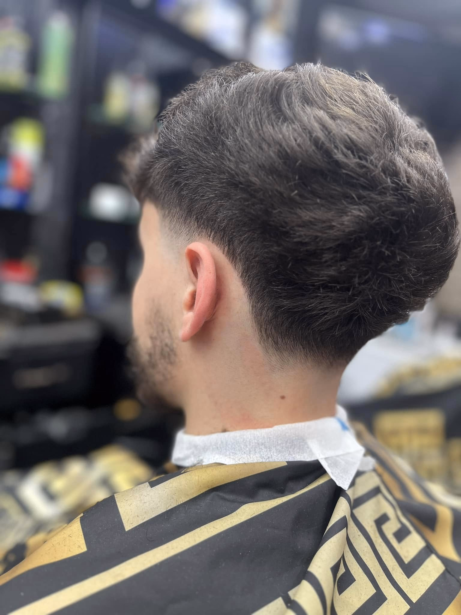 Loose curls left long through the crown over a low taper fade, with a light stubble beard, rear three-quarter view