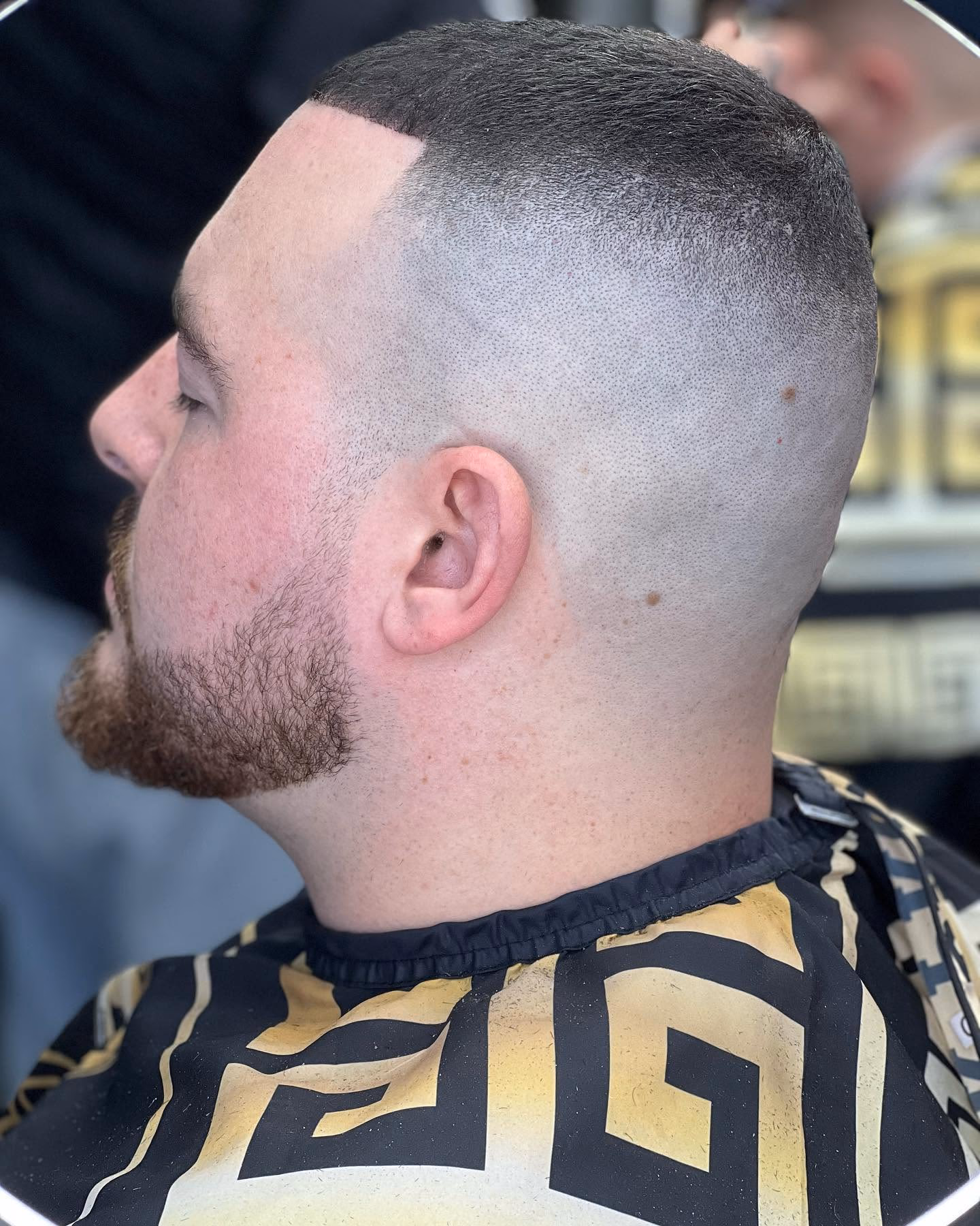 High skin fade with a sharp square line-up, short flat top and a full beard blended into the sides, side profile