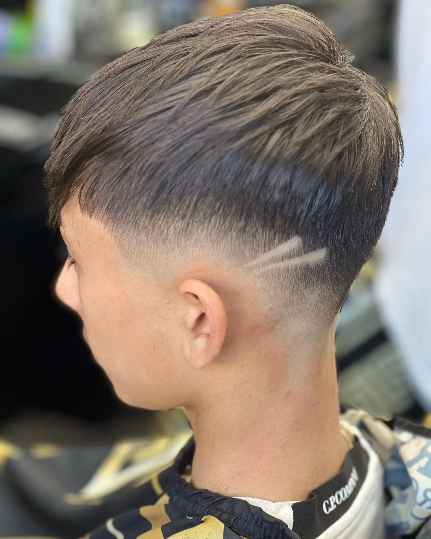 Mid taper fade with an arrow design shaved into the side and a blunt fringe left long on top, side profile
