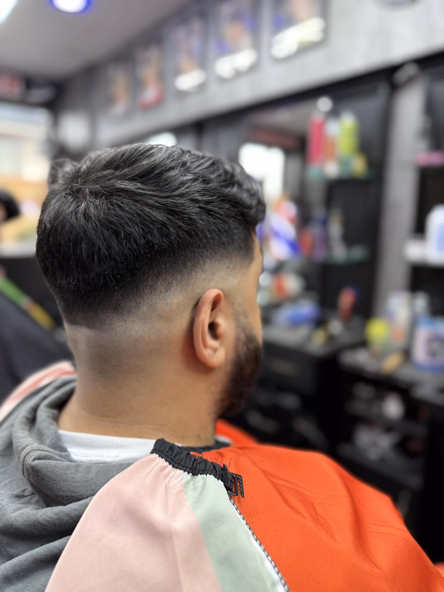 Thick dark hair styled into a quiff over a mid skin fade, with a beard tapered into the fade, rear three-quarter view
